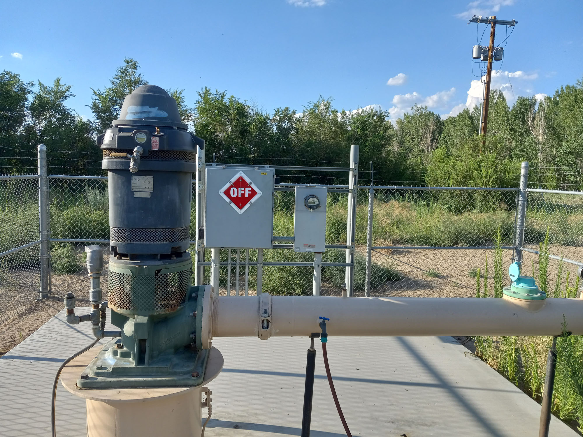 Well W423_2023 07-19_182437 Holly Alpert Electric pump and pipeline near a fenced area; "OFF" sign on electrical panel in background.